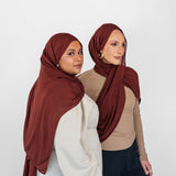 Two women wearing red amber hijabs against a white background