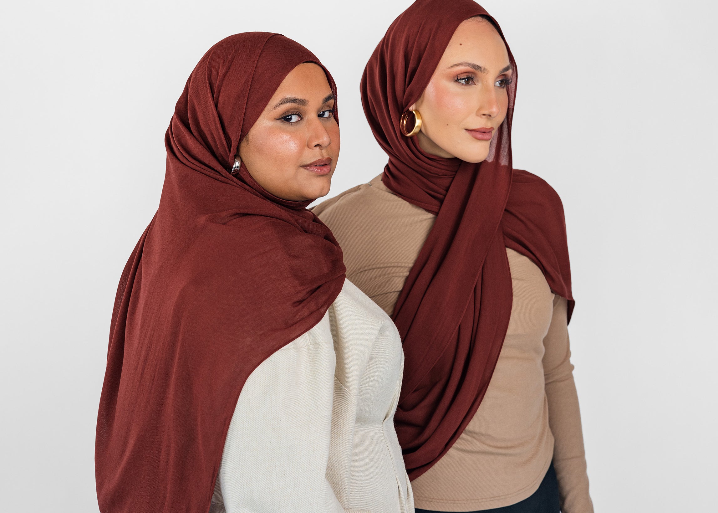 Two women wearing red amber hijabs against a white background