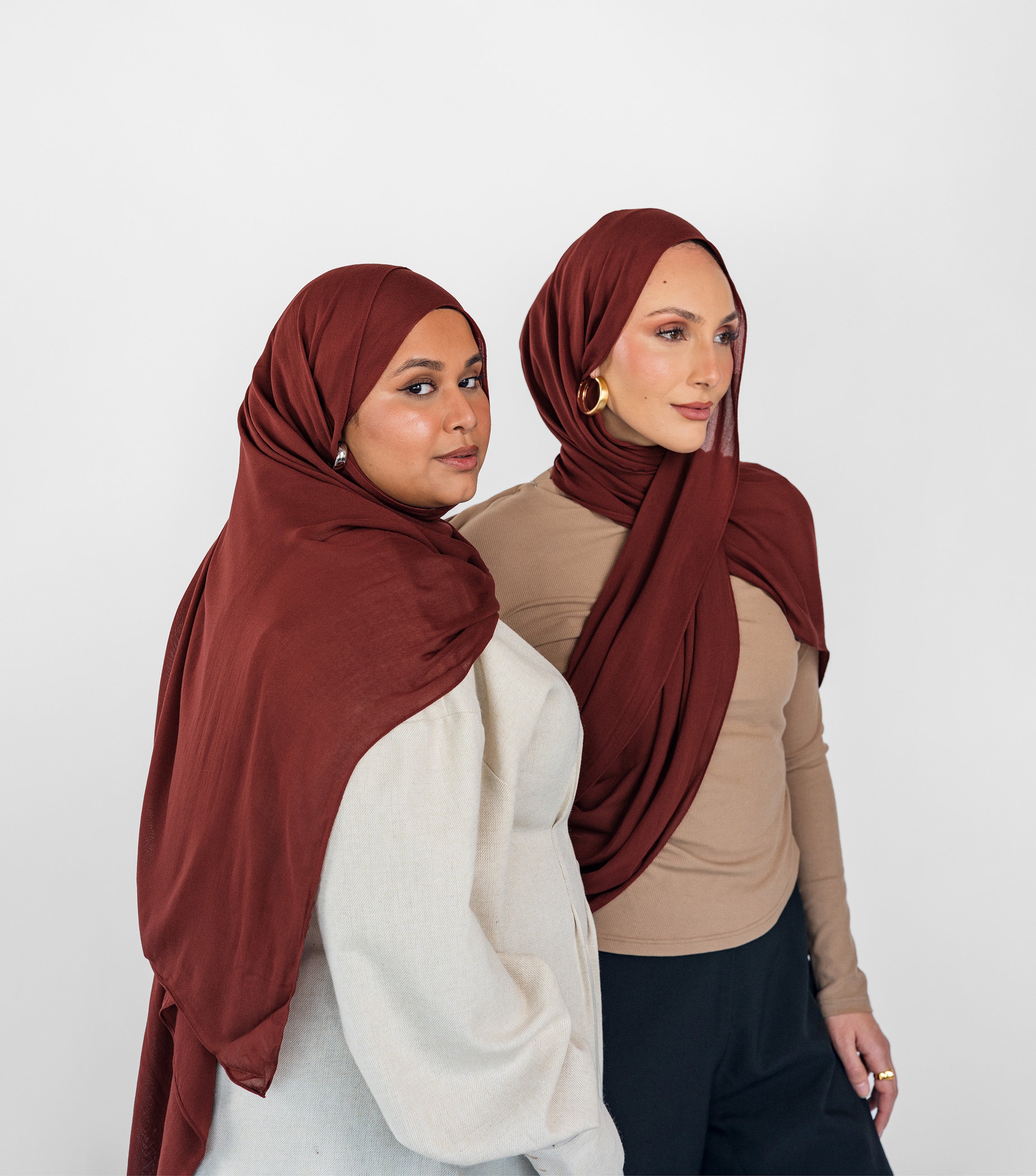 Two women wearing red amber hijabs against a white background