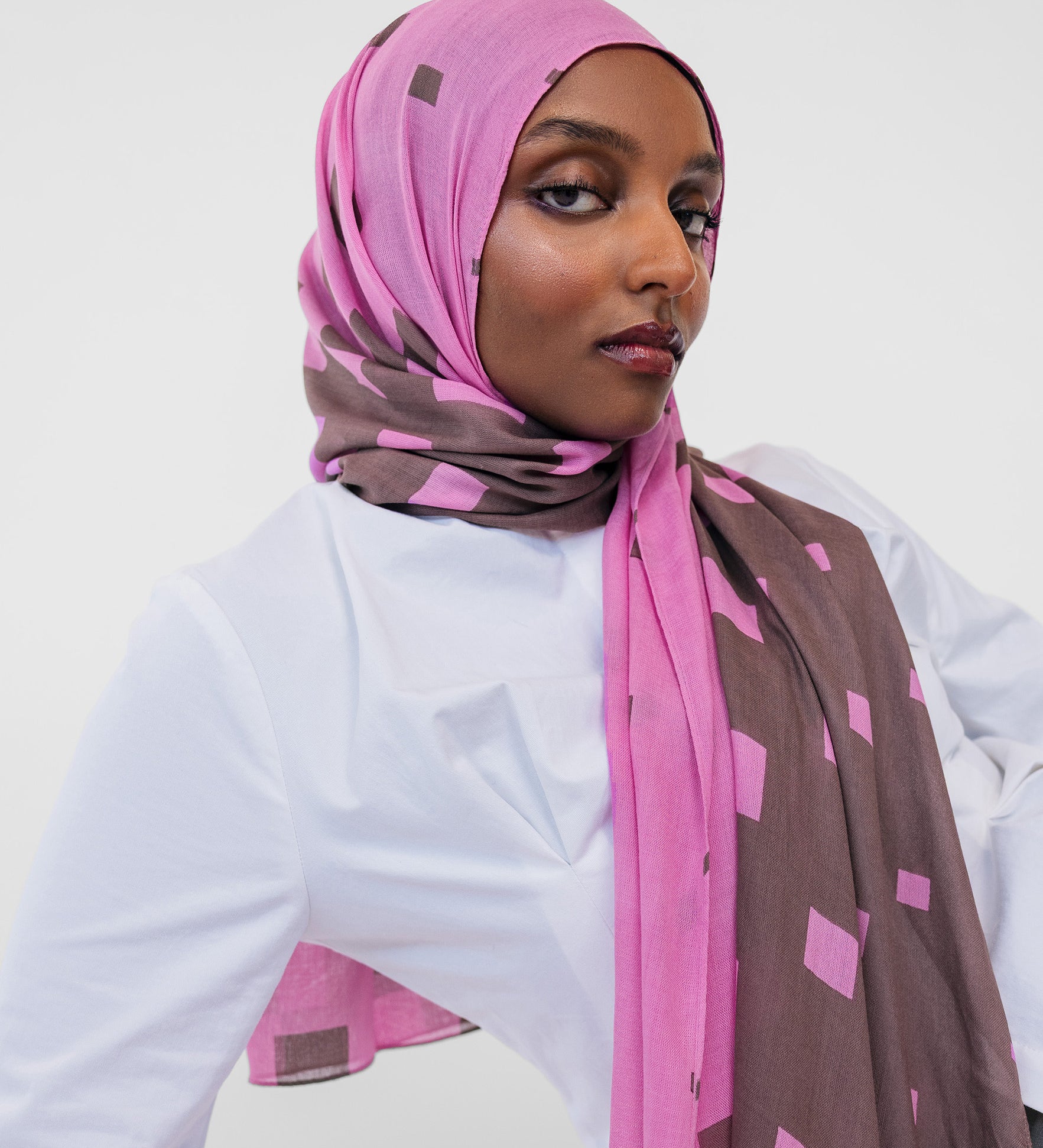 Woman wearing a pink and brown patterned hijab against a white background