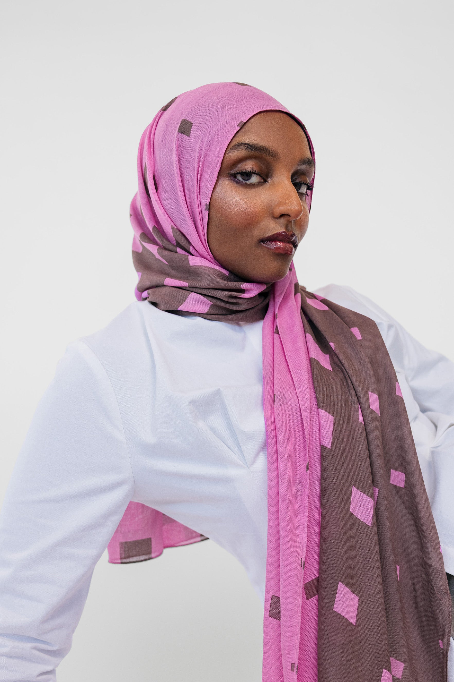 Woman wearing a pink and brown patterned hijab against a white background