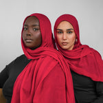 Two women wearing red hijabs against a plain background