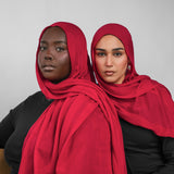 Two women wearing red hijabs against a plain background