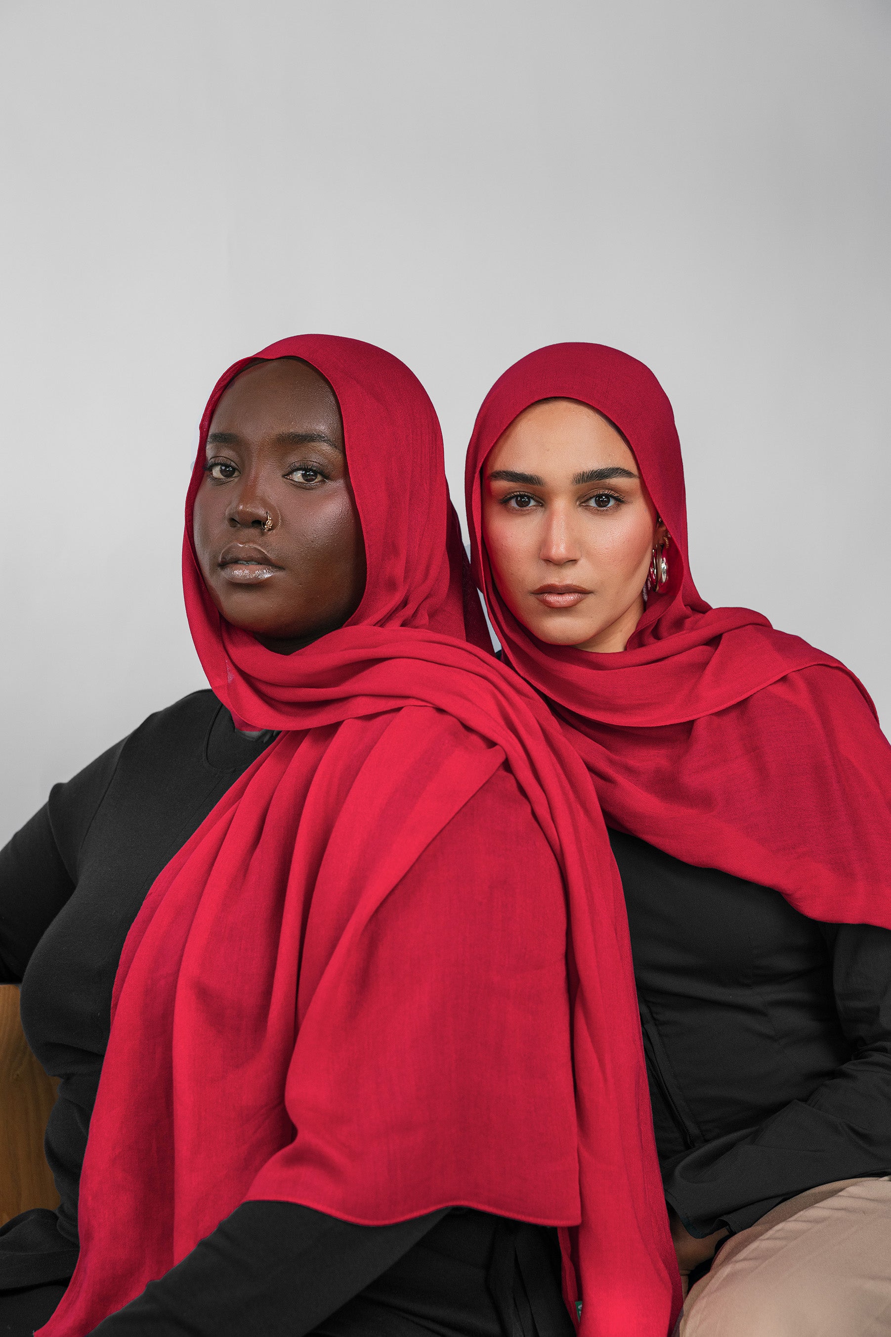 Two women wearing red hijabs against a plain background