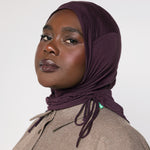 A woman wearing a deep plum purple hijab and taupe button up top