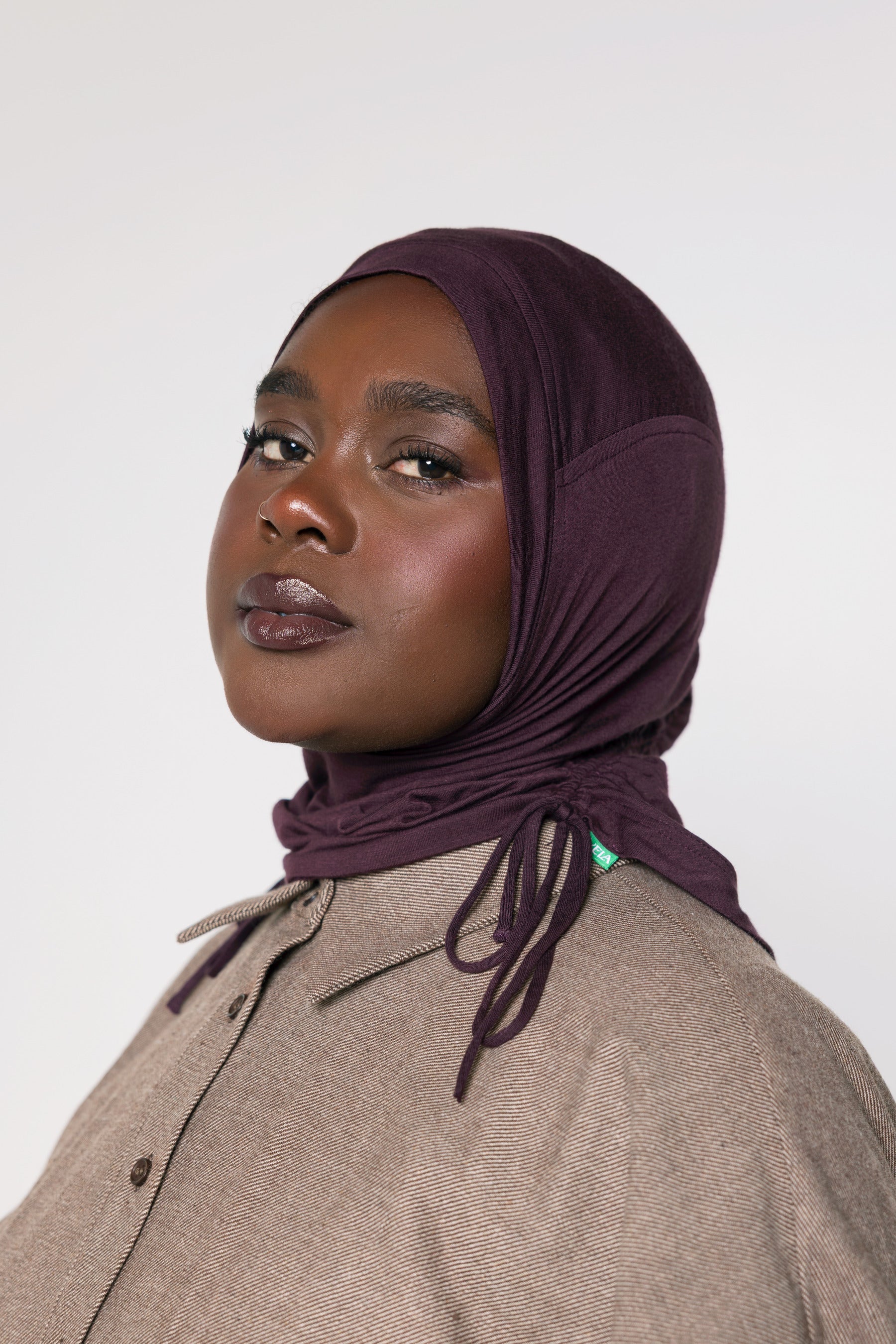 A woman wearing a deep plum purple hijab and taupe button up top