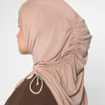 A woman wearing a light beige/tan hijab with ruching and a brown long sleeve top 
