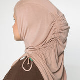 A woman wearing a light beige/tan hijab with ruching and a brown long sleeve top 