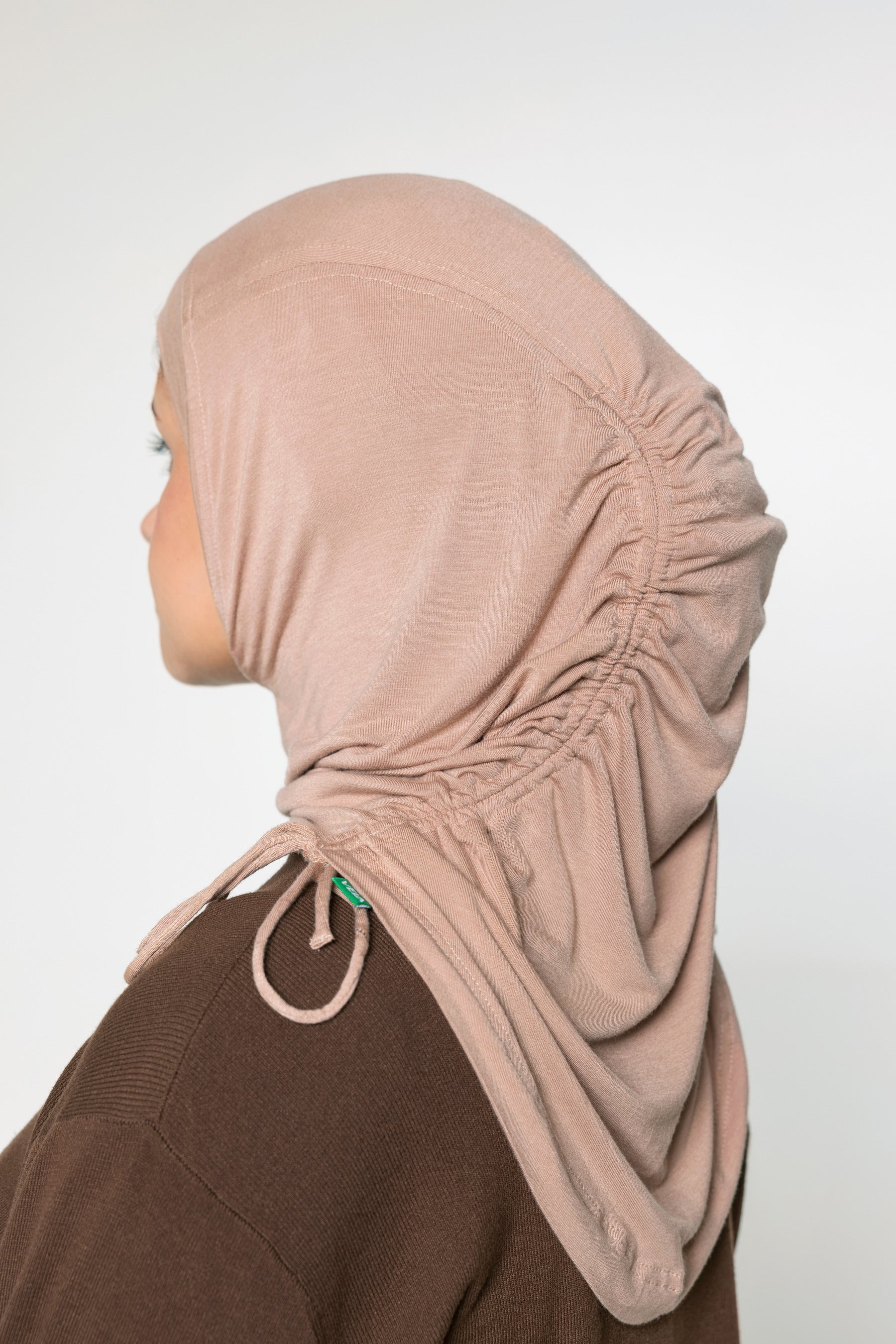 A woman wearing a light beige/tan hijab with ruching and a brown long sleeve top 