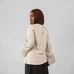 Woman wearing a beige jacket with striped cuffs and a brown hijab on a light gray background