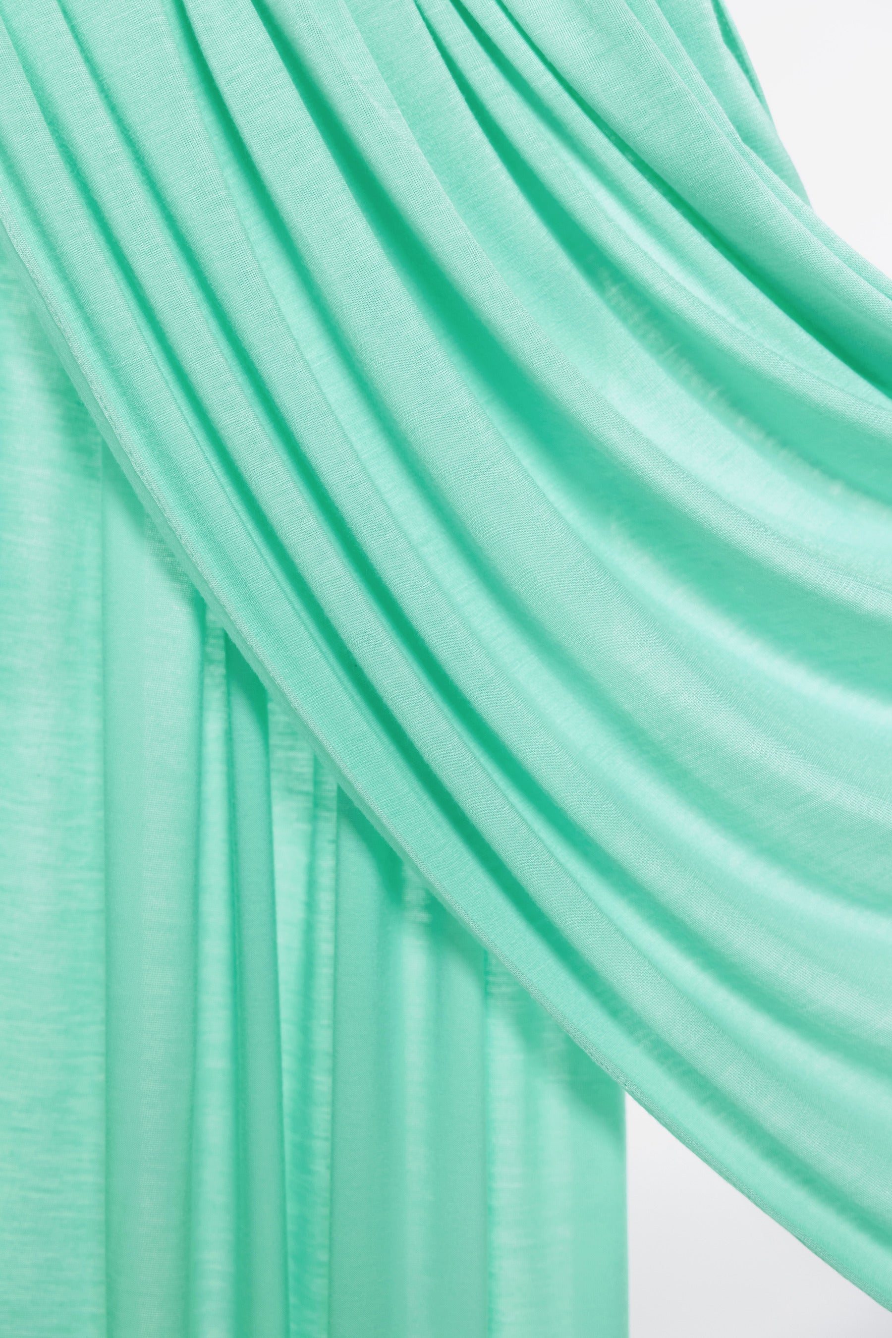 A close-up of draped mint green fabric with soft folds and a subtle sheen, set against a light neutral background.