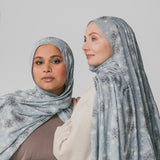 Two women wearing matching light blue hijabs with floral patterns against a plain background