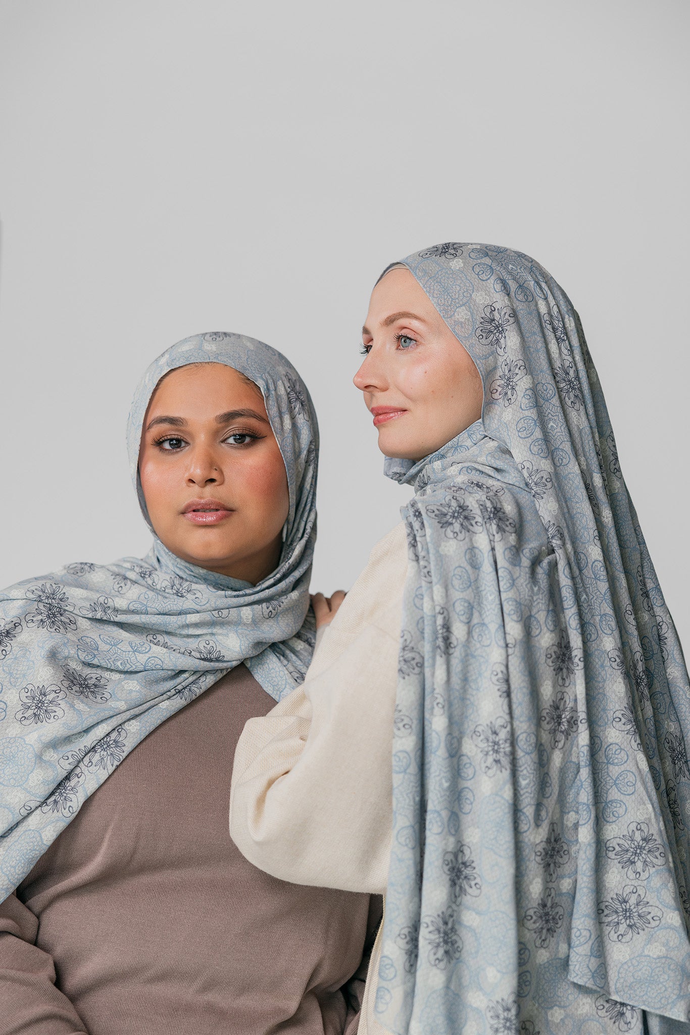 Two women wearing matching light blue hijabs with floral patterns against a plain background