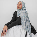 Woman wearing a light blue floral mosaic hijab on a white background