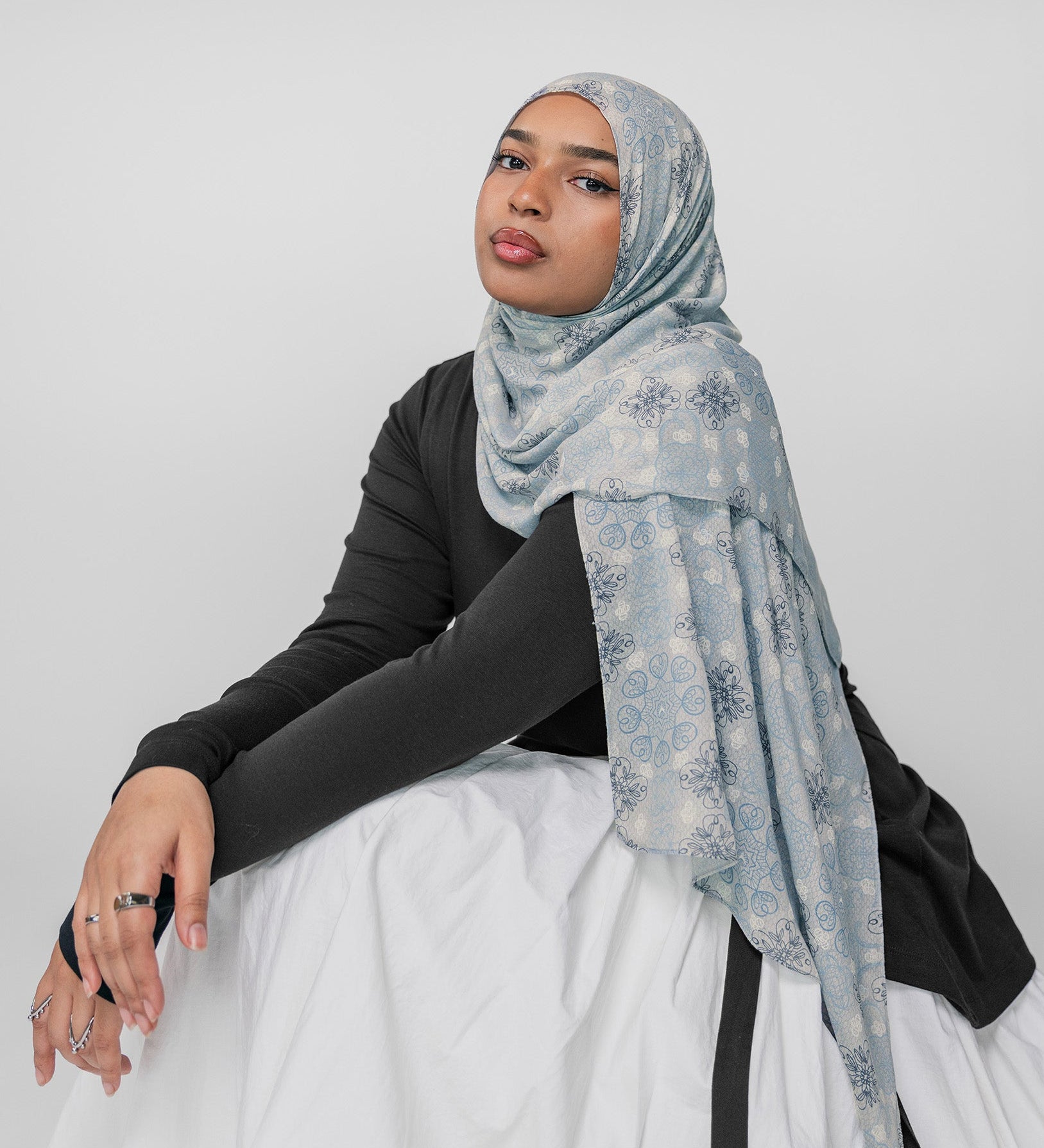 Woman wearing a light blue floral mosaic hijab on a white background