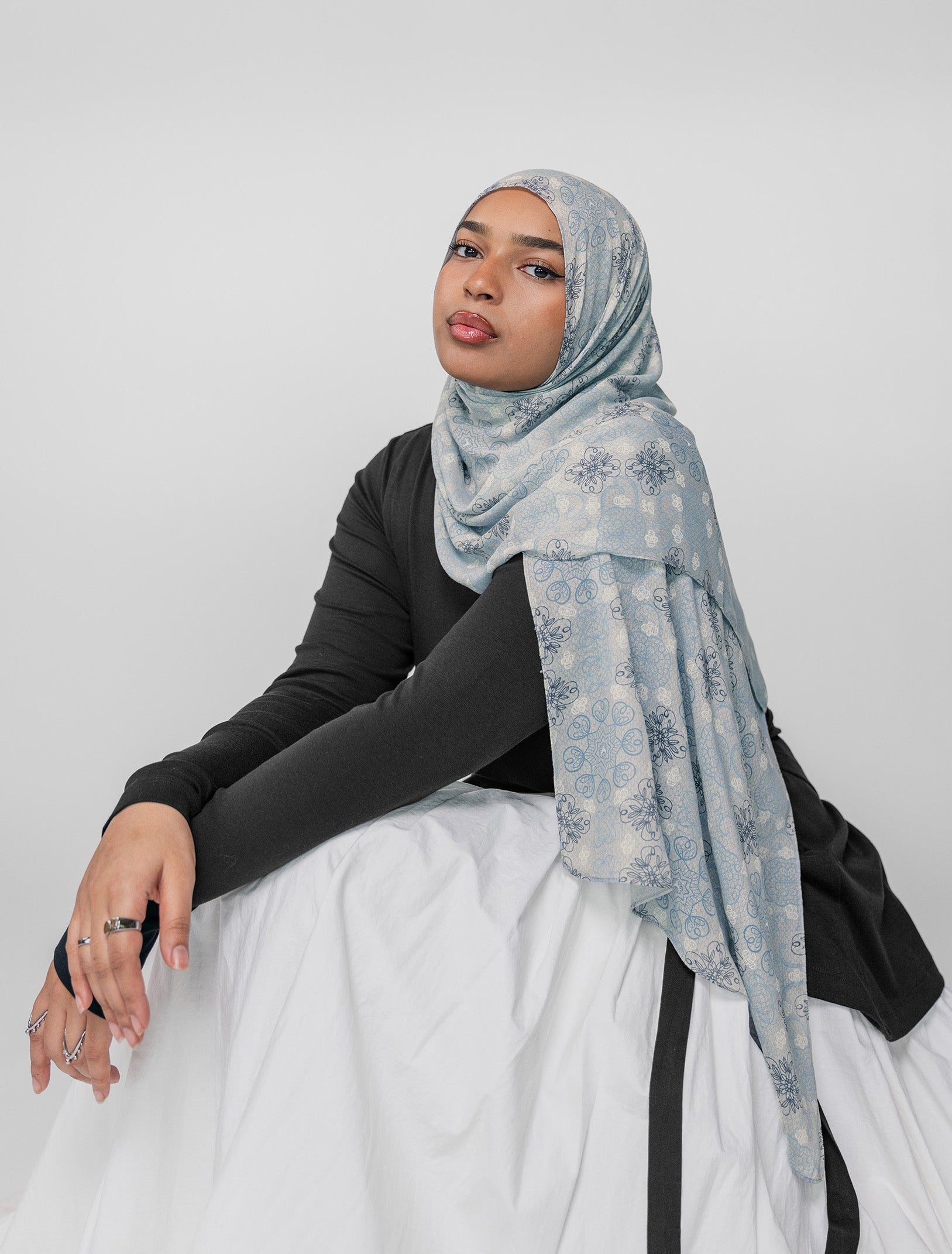 Woman wearing a light blue floral mosaic hijab on a white background