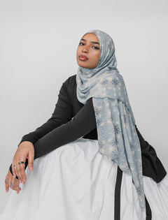 Woman wearing a light blue floral mosaic hijab on a white background