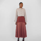 Woman wearing a beige top and rust-colored pleated skirt on a white background