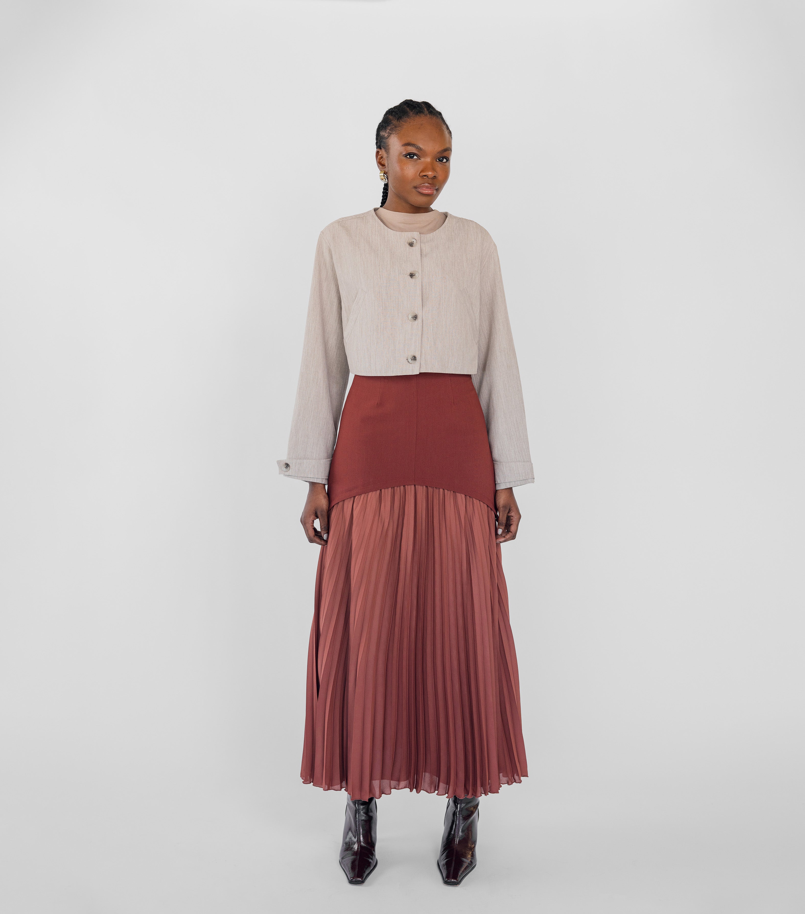 Woman wearing a beige top and rust-colored pleated skirt on a white background