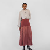 Woman wearing a beige top and red pleated skirt on a white background