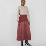 Woman wearing a beige jacket and maroon pleated skirt on a white background
