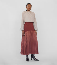 Woman wearing a beige jacket and maroon pleated skirt on a white background