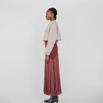 Woman wearing a beige top and red pleated skirt on a white background