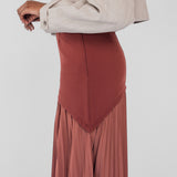 Person wearing a beige blazer and rust-colored pleated skirt on a white background