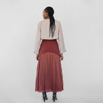 Person wearing a beige jacket and maroon pleated skirt on a white background