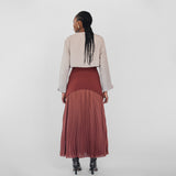Person wearing a beige jacket and maroon pleated skirt on a white background