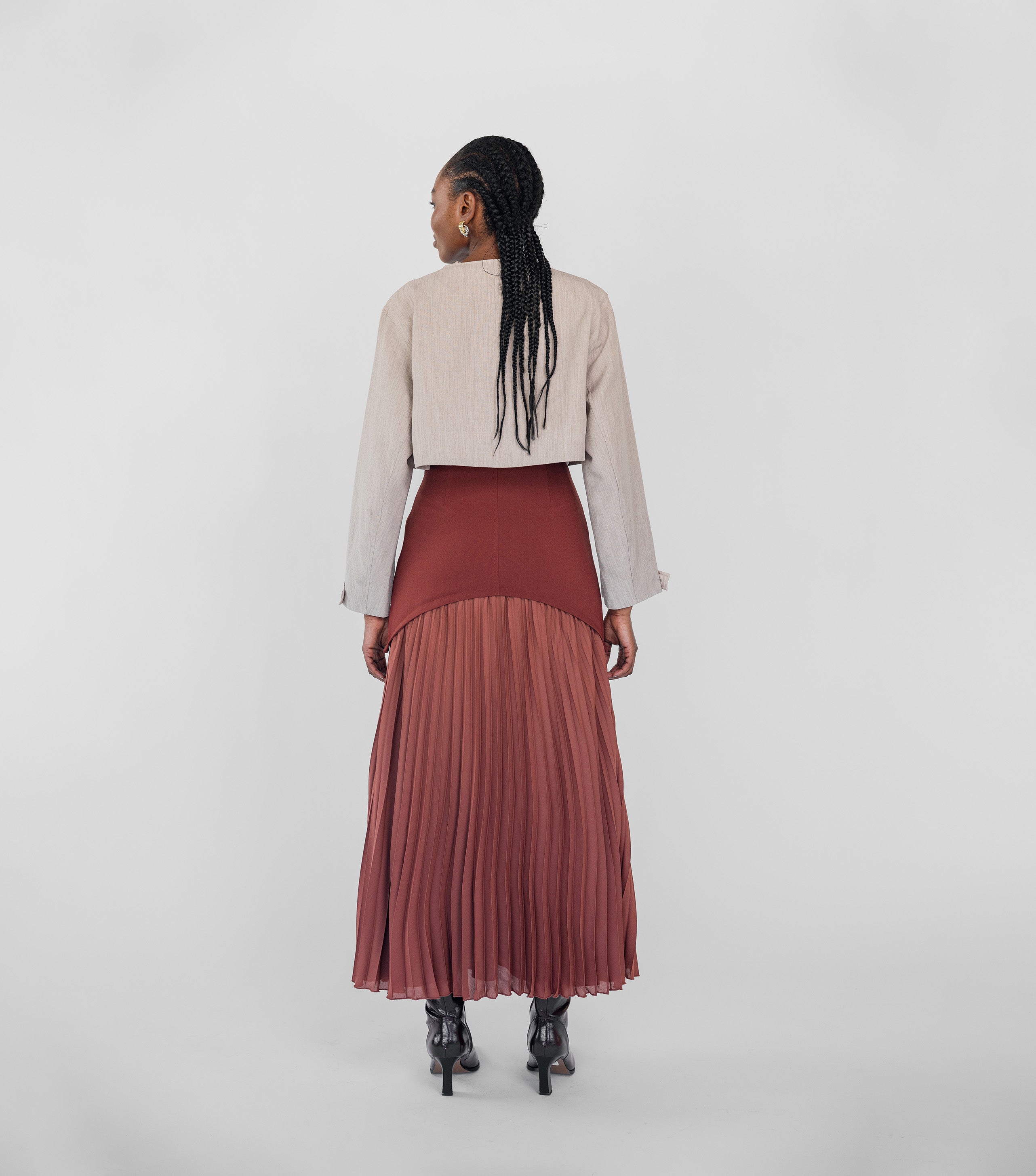 Person wearing a beige jacket and maroon pleated skirt on a white background