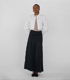 Woman wearing a white jacket and black pleated skirt on a plain background