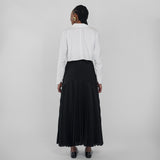 Person wearing a white shirt and black pleated skirt on a plain background