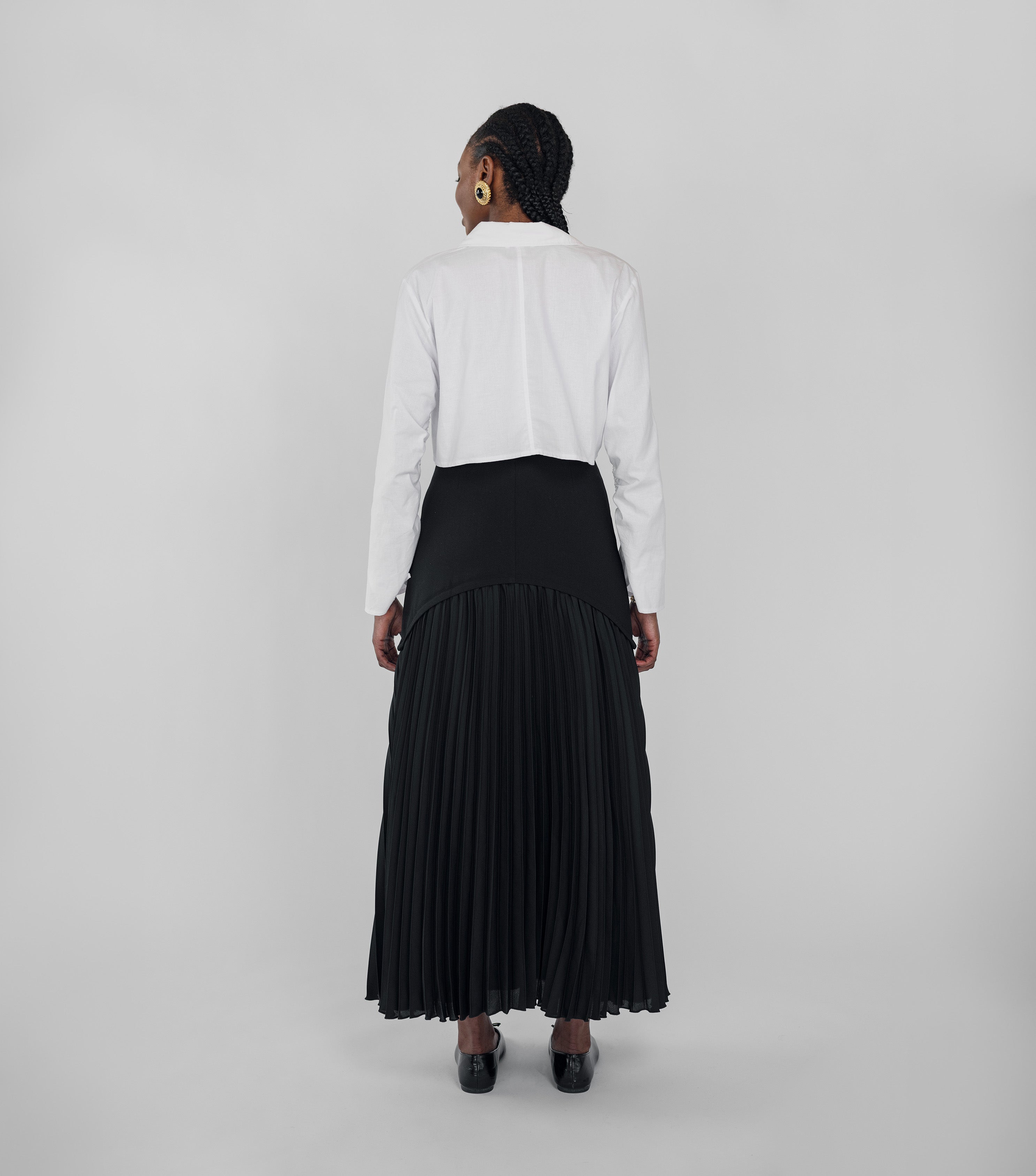 Person wearing a white shirt and black pleated skirt on a plain background