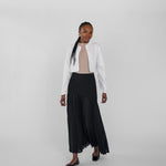 Woman wearing a white jacket and black pleated skirt on a plain background