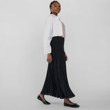 Woman wearing a white blouse and black pleated skirt on a plain background