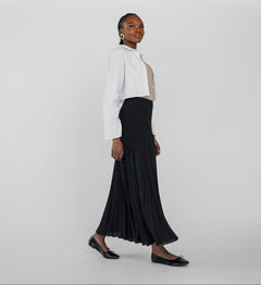 Woman wearing a white blouse and black pleated skirt on a plain background