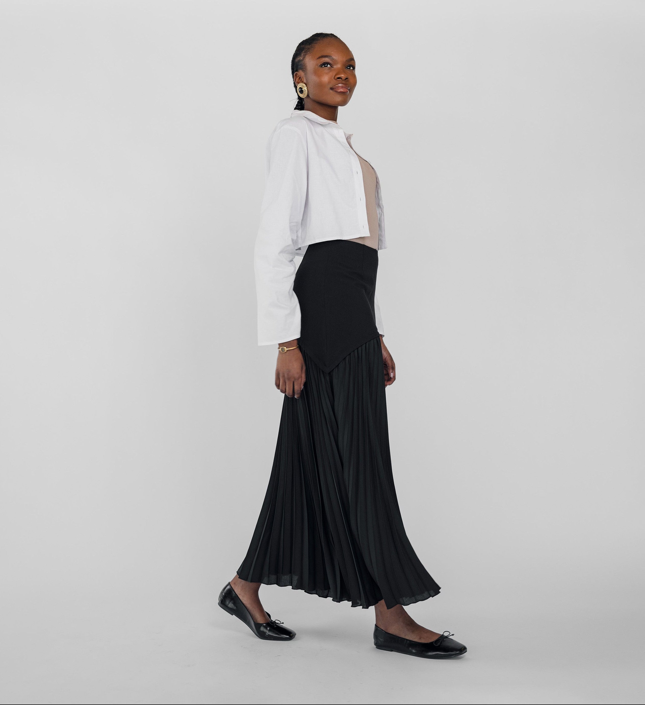 Woman wearing a white blouse and black pleated skirt on a plain background