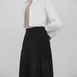 Person wearing a white shirt and black pleated skirt on a plain background