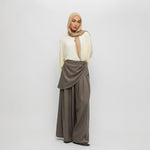 Woman wearing a beige hijab, white top, and brown pants on a white background