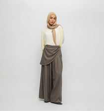 Woman wearing a beige hijab, white top, and brown pants on a white background