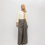 Woman wearing a beige hijab, white top, and gray skirt on a white background