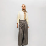Woman wearing a beige hijab, white top, and gray skirt on a white background