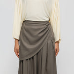 Person wearing a beige top and brown skirt on a plain background