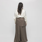 Person wearing a white blouse and brown wide-leg pants on a plain background
