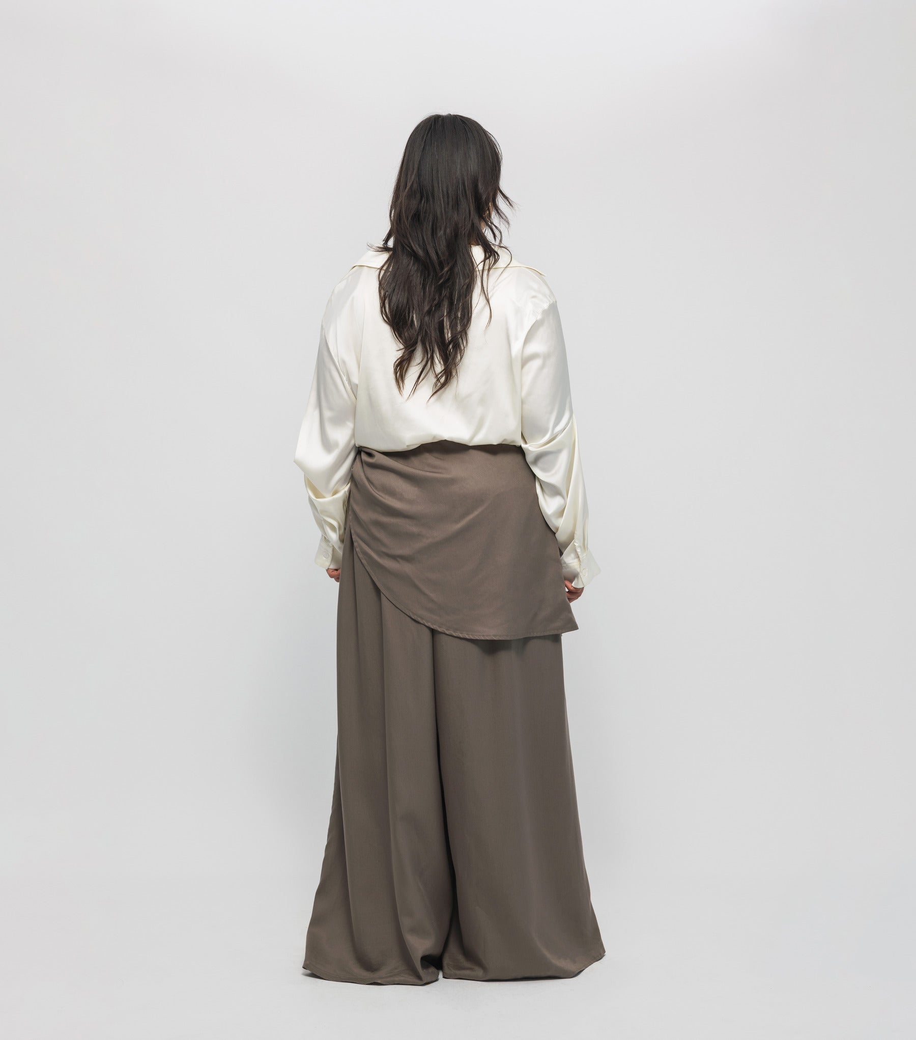 Person wearing a white blouse and brown wide-leg pants on a plain background