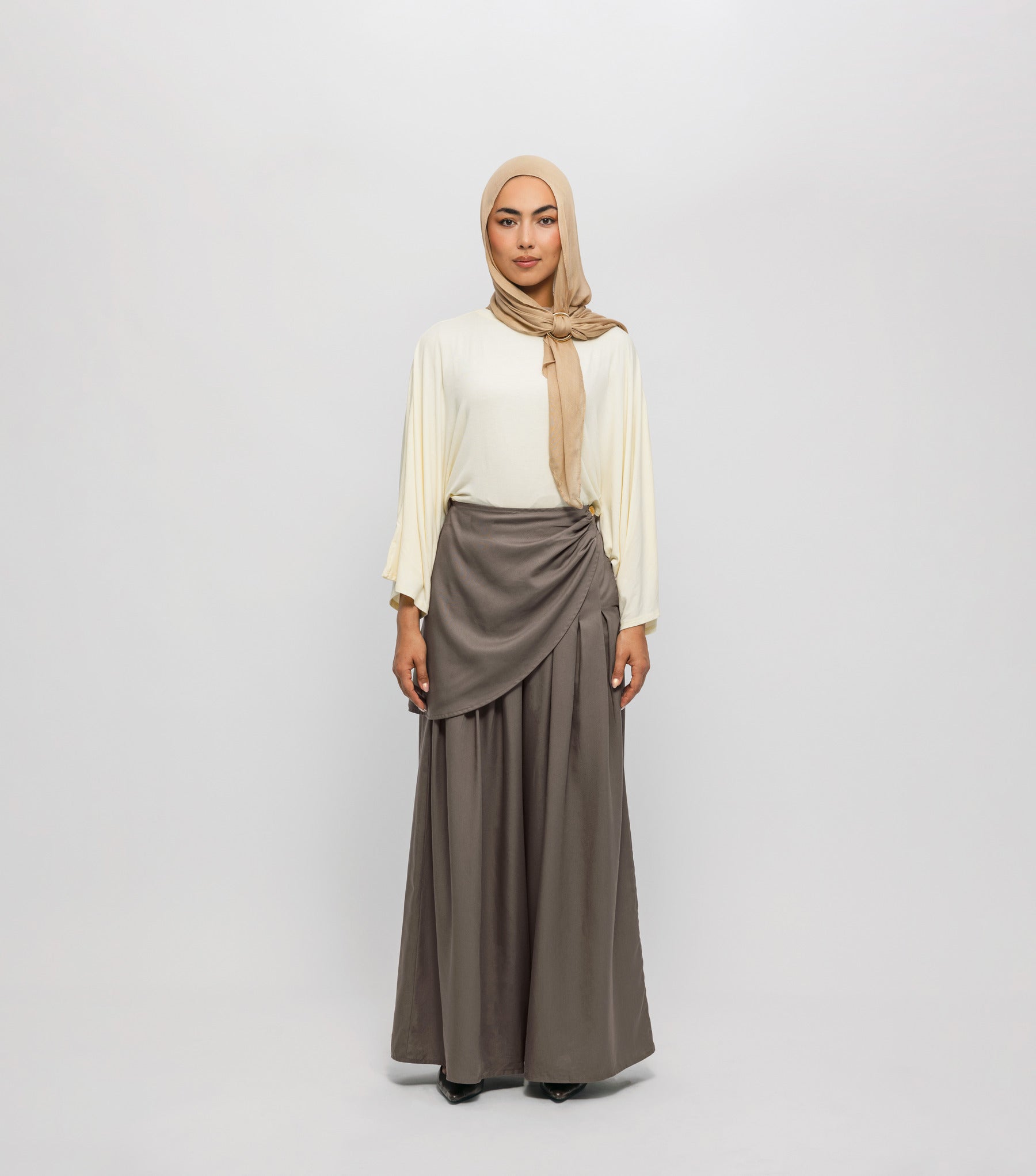 Woman wearing a beige hijab, white blouse, and brown skirt on a white background