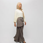 Woman wearing a beige hijab, cream top, and brown skirt on a white background