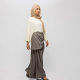 Woman wearing a beige hijab, cream top, and brown skirt on a white background