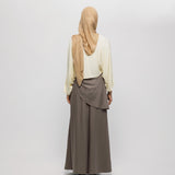 Person wearing a beige hijab and long brown skirt on a white background